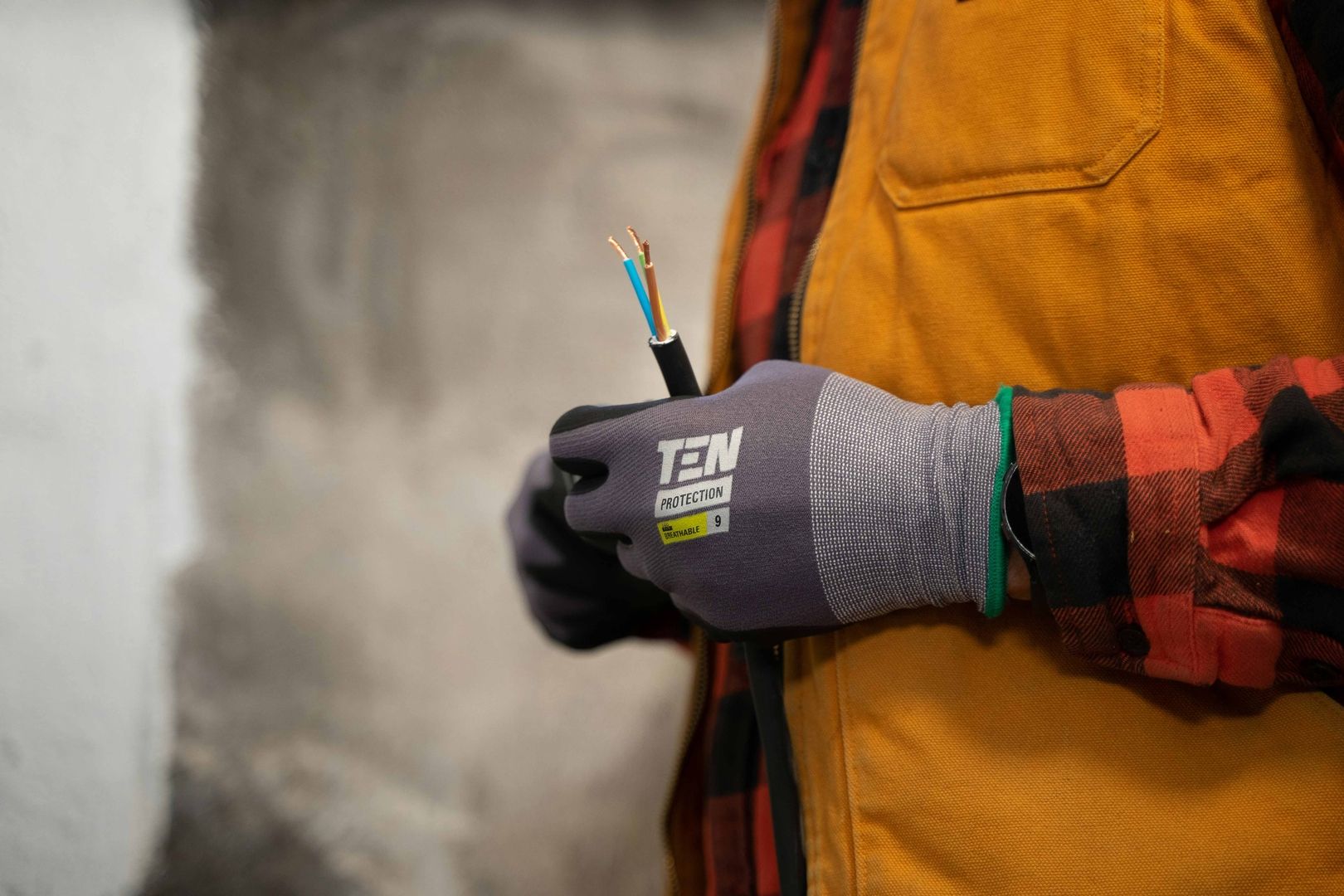 Eine Person mit Handschuhen und oranger Jacke hält ein Stück Elektrokabel mit freiliegenden Drähten.